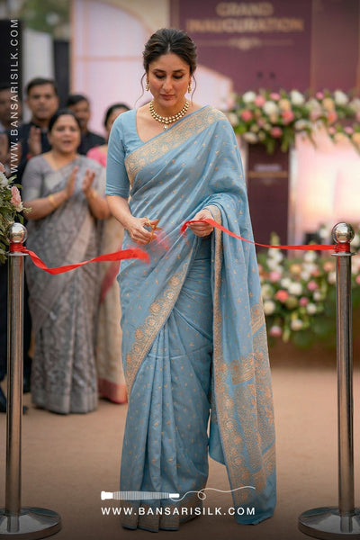 Woman in a light blue saree cutting a red ribbon at an event, with 'Bansari Silk' branding.