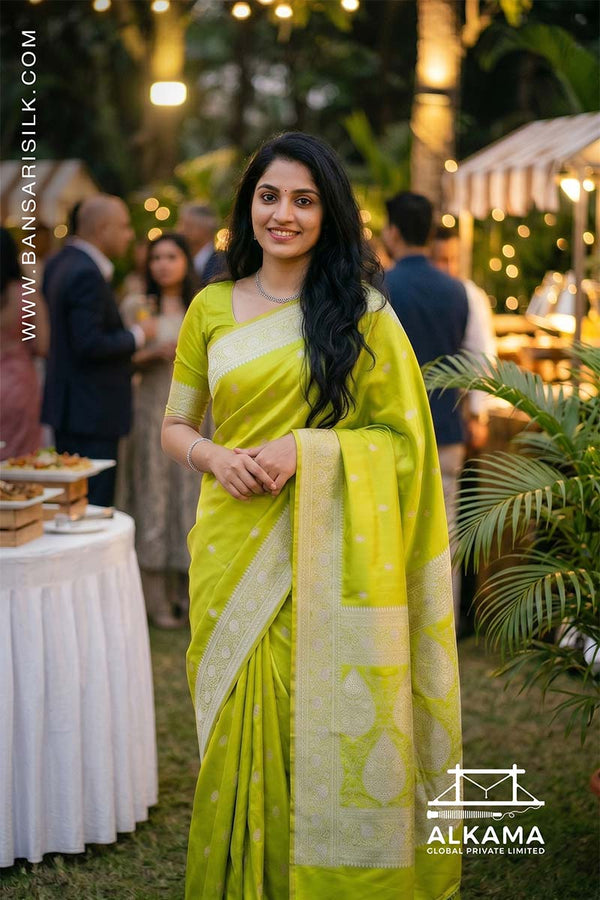 Woman in a liril green Banarasi Mashru silk saree at an outdoor event, with 'ALKAMA' branding.