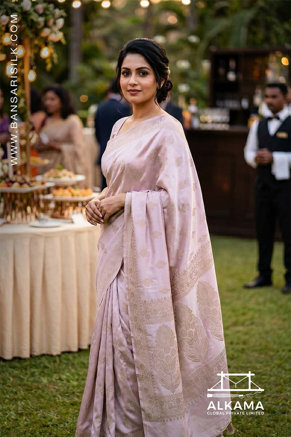 Woman in a lilac-white Banarasi Mashru silk saree at an outdoor event, with 'ALKAMA' branding.