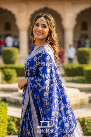 Woman in a blue Banarasi saree with floral patterns standing outdoors.