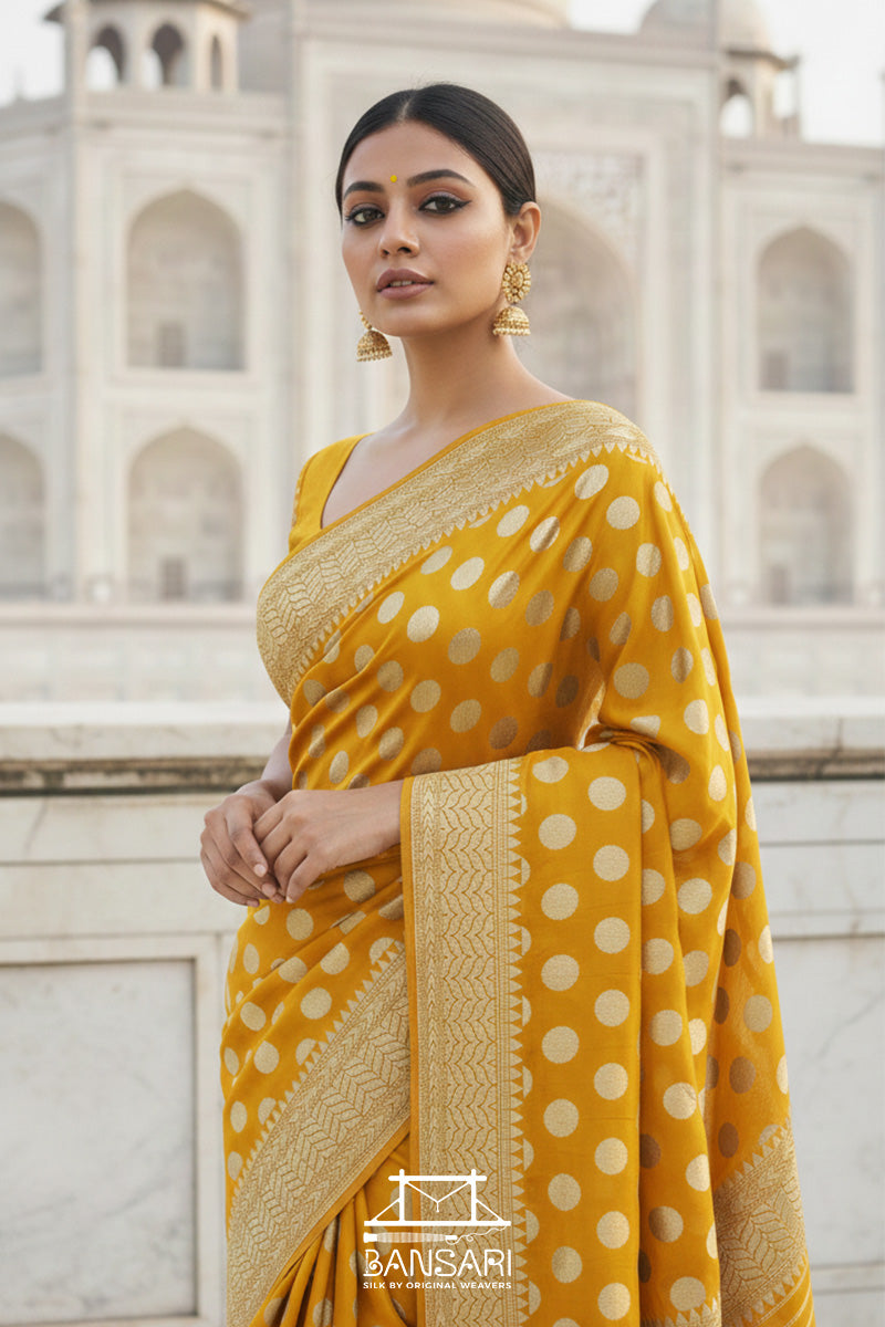 Woman in a yellow Banarasi georgette silk saree with polka dots pattern standing in front of Taj Mahal.