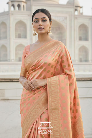 Woman in a peach Banarasi georgette silk saree with gold polka patterns standing in front of the Taj Mahal.