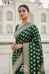 Woman in a bottle green Banarasi georgette silk saree with gold polka patterns standing in front of the Taj Mahal.
