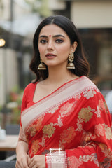 Woman wearing a red Banarasi silk saree with gold patterns, standing outdoors.
