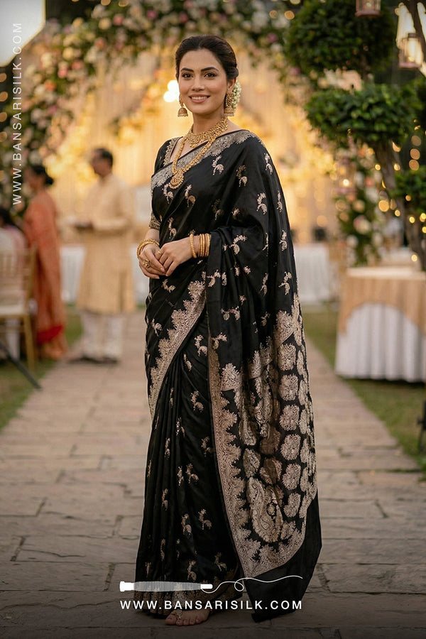 Woman in a black mashru silk saree with gold patterns at an outdoor event.