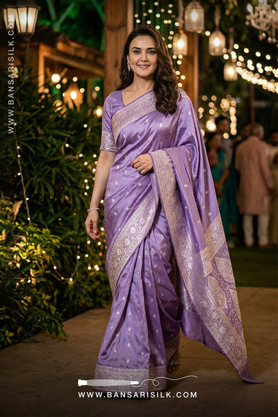 Woman in a purple saree with silver border standing in a decorated outdoor setting.