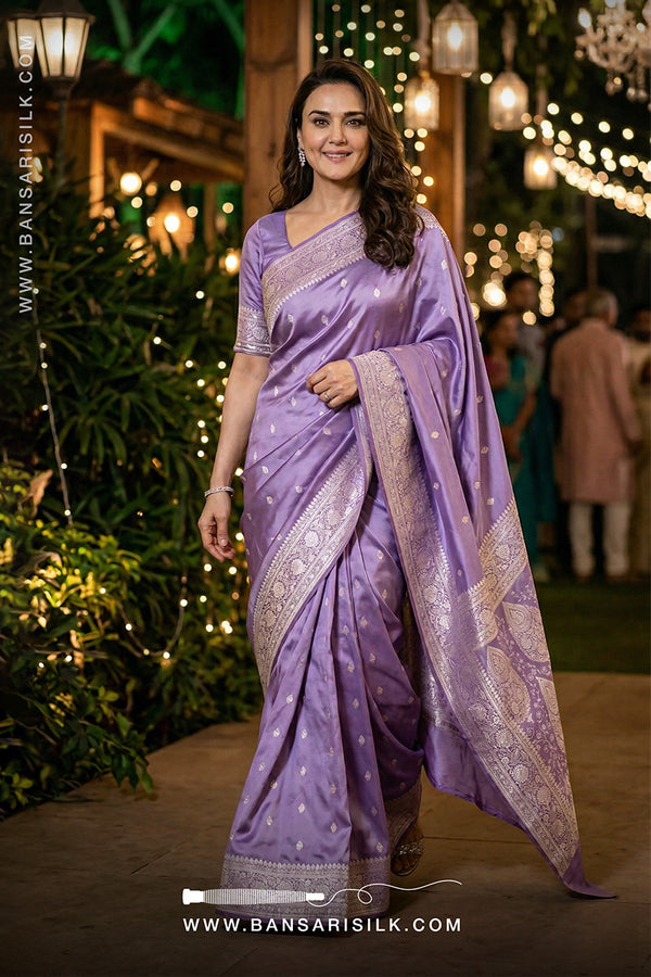 Woman in a purple saree with silver border standing in a decorated outdoor setting.